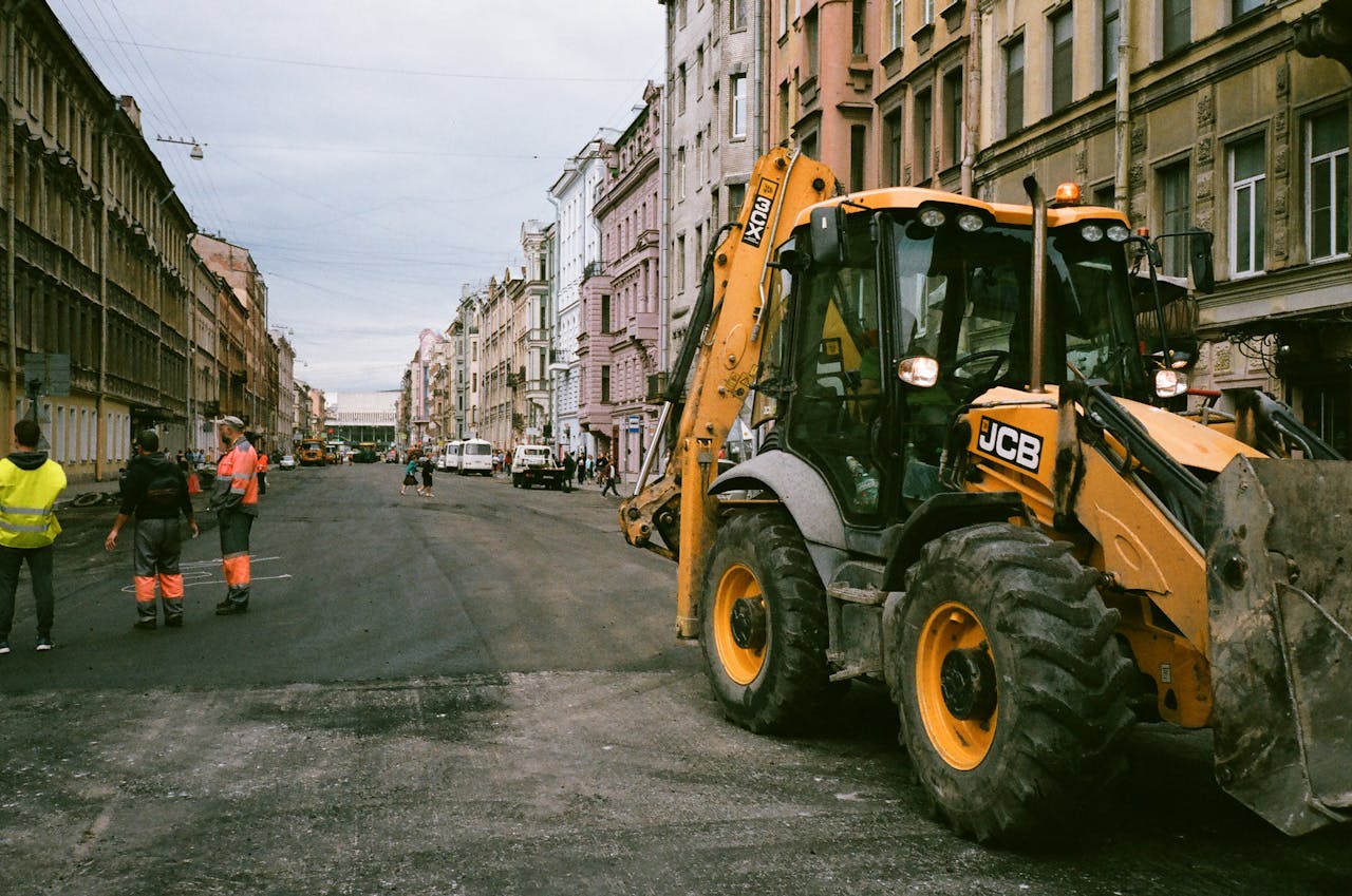 our-services-1 City street construction scene with workers and JCB excavator.