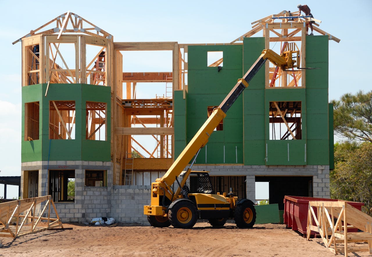 hero-img-01 A multi-story wooden house under construction using a crane on a sunny day.